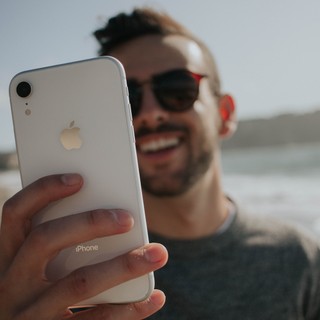 Man smiles in sunglasses while looking at his iPhone