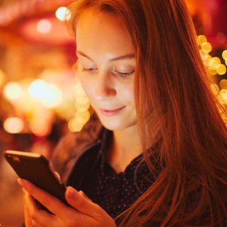 Girl checks phone amid fairy lights at nighttime