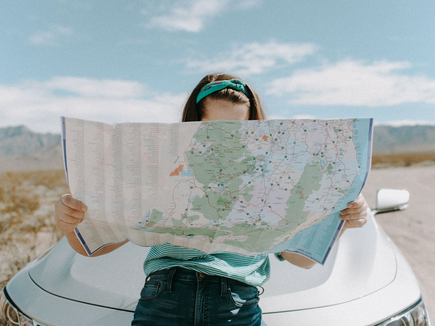 how-to-find-travel-insurance-woman-leaning-on-car-looking-at-a-map